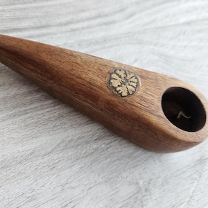 May include: A handcrafted wooden pipe with a smooth, polished finish. The pipe is a rich brown color and features a decorative inlay with a floral design. The bowl is a dark, circular opening. The pipe is approximately 5 inches long.