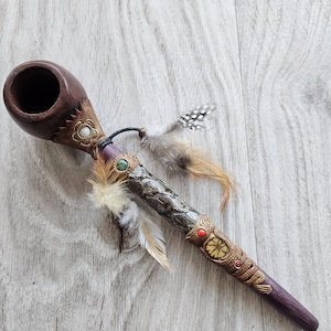 May include: A handcrafted wooden pipe with a dark brown bowl and a long, decorated stem. The stem features ornate carvings, faux gemstones, and decorative feathers. The pipe is designed with a Native American aesthetic.