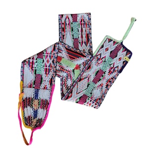 May include: A colorful, patterned textile with a geometric design. The textile features a mix of vibrant colors including pink, green, red, and white. The textile has a fringed edge and a loop at one end.