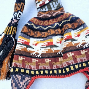 Könnte beinhalten: Eine bunte Strickmütze mit einem langen Bommel. Die Mütze hat ein geometrisches Muster mit Lamas und anderen Tieren. Die Mütze ist aus Wolle und fühlt sich warm und gemütlich an.