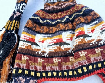 May include: A colorful knitted hat with a long tassel. The hat features a geometric pattern with llamas and other animals. The hat is made of wool and has a warm, cozy feel.