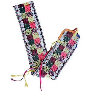 May include: Two colorful, patterned fabric tubes with tassels. The tubes feature a geometric design in various colors, including pink, green, yellow, and purple. The fabric appears to be woven with a detailed pattern. One tube is partially unrolled, revealing the interior.