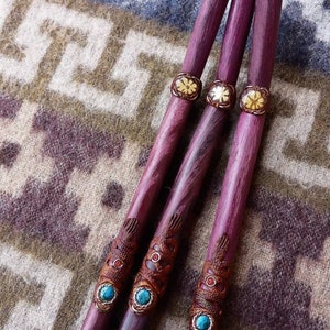May include: Three wooden sticks with decorative carvings and turquoise and gold accents. The sticks are purple and have a wood grain pattern.