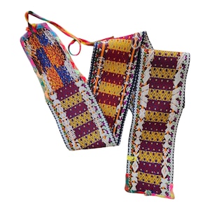 May include: A colorful woven belt with intricate patterns in shades of red, yellow, blue, and white. The belt features geometric designs and a long, braided tie. The ends are finished with decorative stitching and a small tag.