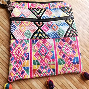 Könnte beinhalten: Eine bunte Stofftasche mit mehreren Mustern, zwei Reißverschlussfächern und Quasten. Die Tasche ist aus einem gewebten Stoff mit einem geometrischen Muster in den Farben Rosa, Blau, Grün, Gelb und Weiß.