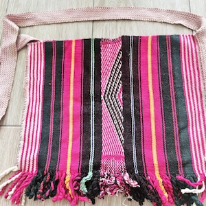 Peut inclure: Sac à bandoulière tissé avec un motif rayé rose, noir et blanc. Le sac est doté d'une bandoulière tissée et d'un fond à franges. Le design comprend un motif géométrique central. Le sac est en tissu tissé.
