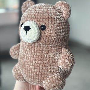 Könnte beinhalten: Ein handgefertigter Teddybär in einem weichen, gedämpften Braunton. Der Bär hat eine weiße, strukturierte Schnauze mit einer schwarzen Nase und zwei schwarzen Augen. Der Körper des Bären ist abgerundet, mit kleinen Armen, Beinen und Ohren.