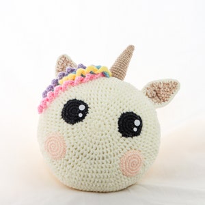Könnte beinhalten: Ein weißes, gehäkeltes Stofftier in Form eines Einhorns mit einer Regenbogenmähne und einem Horn. Das Einhorn hat schwarze Augen und rosafarbene Wangen.