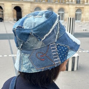 May include: A patchwork denim bucket hat in various shades of blue. The hat features a mix of denim pieces, some with frayed edges, and a small patch of white polka dots on a blue background. The hat has a unique, handcrafted appearance.