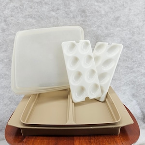 Könnte beinhalten: Ein Vintage-Tupperware-Set mit einem geteilten Serviertablett in Beige, einem transparenten Deckel und zwei weißen Eierhaltern. Das Set besteht aus strapazierfähigem Kunststoff und ist für die Aufbewahrung und das Servieren von Lebensmitteln konzipiert.