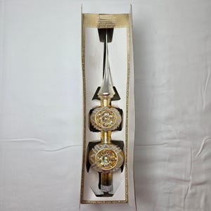 May include: A vintage glass Christmas tree topper in a tall, pointed shape with a gold and silver finish. It features two spherical sections decorated with glittery patterns and central indentations. The ornament is housed in its original box.