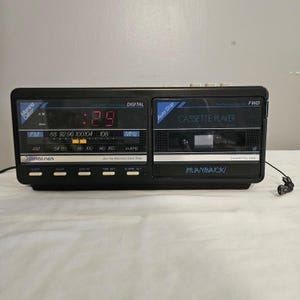 May include: Black Soundesign AM/FM radio and cassette player with a digital clock display. The clock shows 7:29 in red digits. Features include an auto-stop cassette player and FM/AM radio frequencies.