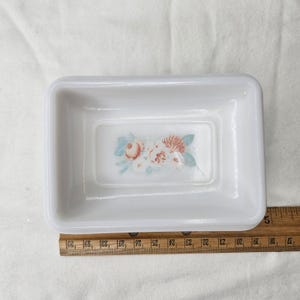 May include: A rectangular white dish with a floral design in the center. The design features pink, peach, and blue flowers. The dish is approximately 5 inches long.