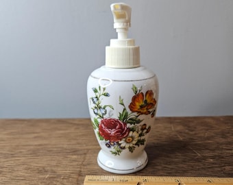 Dispensador de jabón de cerámica vintage con diseño floral de rosas blancas y detalles plateados, estilo shabby chic.