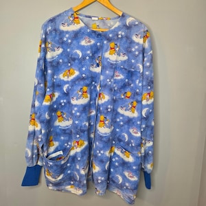 Könnte beinhalten: Ein langärmeliges, blaues Schlupfkasack-Oberteil mit Knopfleiste und einem durchgehenden Muster aus Winnie Puuh und I-Aah, die auf Wolken ruhen, umgeben von weißen Sternen und Mondsicheln. Das Oberteil verfügt über eine Brusttasche und blaue Bündchen.