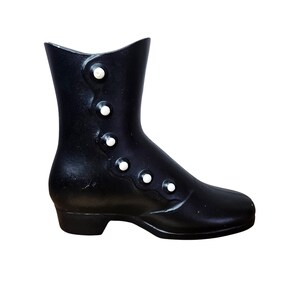 May include: A black boot with a rounded toe and a small heel. The boot has a series of white, round buttons running down the side. The top of the boot has a slight curve. The boot is a decorative item.