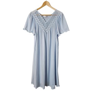 May include: A light blue nightgown featuring short flutter sleeves and a V-neckline adorned with white floral lace trim. The garment is displayed on a wooden hanger, showcasing a loose, flowing silhouette with a scalloped hemline detail.