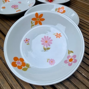 Könnte beinhalten: Vier weiße Keramikschalen mit einem Blumendesign in Orange-, Rosa- und Grüntönen. Die Schalen sind übereinander gestapelt.