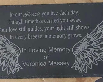 May include: A rectangular black slate plaque featuring engraved angel wings on the left and right sides. The center text reads: In our Hearts you live each day, Though time has carried you away. Your love still guides, your light still shows, In every breeze, a memory grows. In Loving Memory of Veronica Massey.