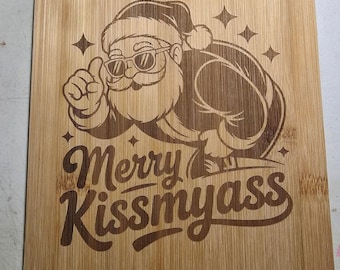 May include: A rectangular bamboo cutting board featuring a laser-engraved illustration of Santa Claus wearing sunglasses and giving a thumbs up. Below the figure, the text reads Merry Kissmyass, accompanied by small four-pointed star accents.