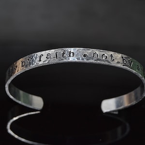 May include: A silver bracelet with the words "by faith, not by sight" engraved on it.