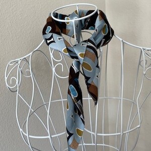 Puede incluir: Una bufanda con estampado azul y marrón con formas geométricas en un maniquí de alambre blanco.