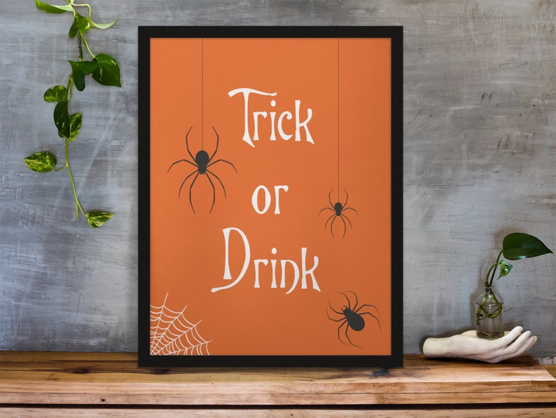 K&ouml;nnte beinhalten: Ein gerahmtes orangefarbenes Poster mit dem Text "Trick or Drink" in Wei&szlig;. Es befinden sich drei schwarze Spinnen-Silhouetten, die von der Oberseite des Posters h&auml;ngen. In der linken unteren Ecke befindet sich ein Spinnennetz.