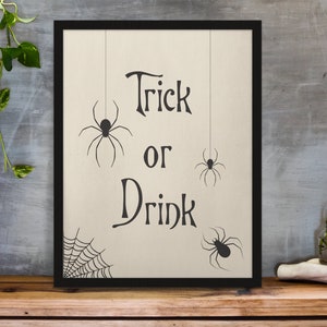 K&ouml;nnte beinhalten: Ein gerahmter Druck mit dem Text "Trick or Drink" in einer dekorativen Schriftart. Drei schwarze Spinnen-Silhouetten h&auml;ngen oben am Druck. Ein Spinnennetz-Design befindet sich unten am Druck.
