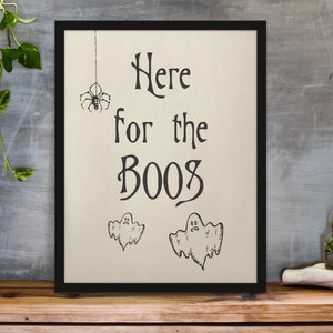 K&ouml;nnte beinhalten: Ein schwarzer gerahmter Druck mit wei&szlig;em Hintergrund. Der Druck sagt "Here for the Booos" mit einer Spinne und zwei Geistern, die darauf gezeichnet sind.