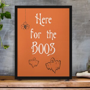 K&ouml;nnte beinhalten: Orangefarbener gerahmter Druck mit dem Text "Here for the boos" in Wei&szlig;. Der Druck zeigt eine Spinne, die an einer Schnur h&auml;ngt, und zwei Geister.