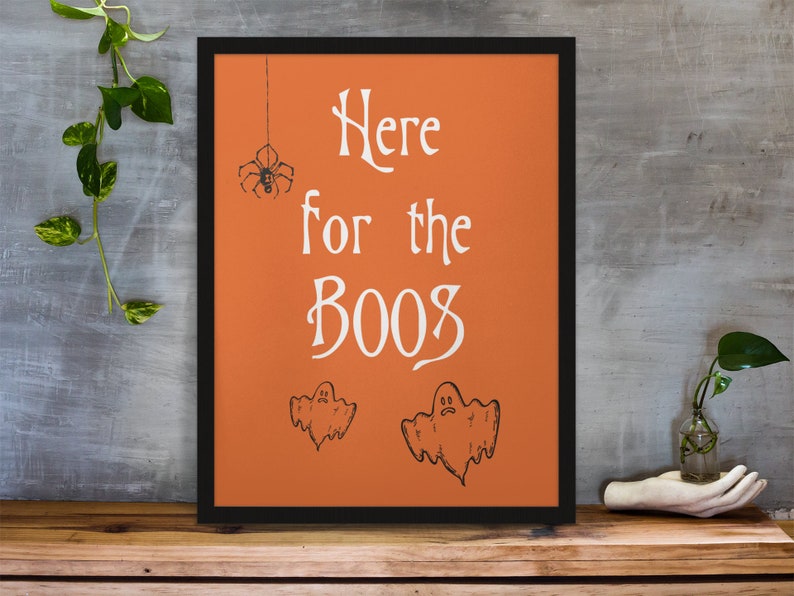 K&ouml;nnte beinhalten: Orangefarbener gerahmter Druck mit dem Text "Here for the boos" in Wei&szlig;. Der Druck zeigt eine Spinne, die an einer Schnur h&auml;ngt, und zwei Geister.