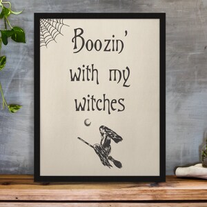 K&ouml;nnte beinhalten: Ein schwarzer gerahmter Druck mit dem Text "Boozin' with my witches" und einer Schwarzwei&szlig;illustration einer Hexe, die auf einem Besen fliegt.