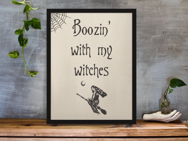K&ouml;nnte beinhalten: Ein schwarzer gerahmter Druck mit dem Text "Boozin' with my witches" und einer Schwarzwei&szlig;illustration einer Hexe, die auf einem Besen fliegt.