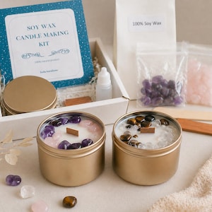 Puede incluir: Un kit para hacer velas de cera de soja con dos botes dorados llenos de cera blanca y piedras decorativas. El kit incluye una caja con la etiqueta "Soy Wax Candle Making Kit", cera de soja y otros suministros.