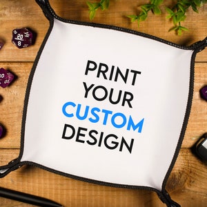 Pode incluir: Uma bandeja de dados branca com borda preta. A bandeja tem o texto "PRINT YOUR CUSTOM DESIGN" impresso nela em letras pretas e azuis. A bandeja é cercada por dados roxos com vários números.