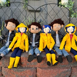 May include: Five plush dolls, including three wearing yellow raincoats, sitting on a brick wall. The dolls have black hair, brown eyes, and are wearing jeans and jackets.