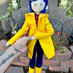 May include: A handmade doll wearing a yellow raincoat, blue jeans, and yellow rain boots. The doll has blue yarn hair, a red and white striped shirt, and a butterfly hair clip.