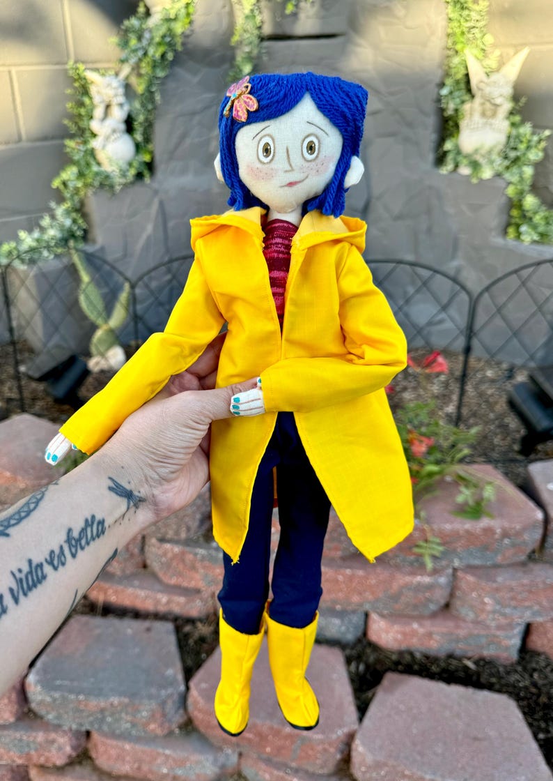 May include: A handmade doll wearing a yellow raincoat, blue jeans, and yellow rain boots. The doll has blue yarn hair, a red and white striped shirt, and a butterfly hair clip.