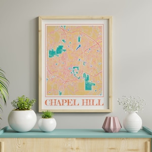 May include: A framed print of a map of Chapel Hill, North Carolina. The map is in a retro style with a yellow background and green and pink lines. The text "Chapel Hill" is printed in orange at the bottom of the map.