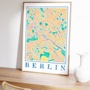 Może przedstawiać: Wydruk w ramie kolorowej mapy Berlina, Niemcy. Mapa jest w odcieniach ż&oacute;łtego, pomarańczowego, zielonego i niebieskiego. Słowo "BERLIN" jest nadrukowane na dole mapy kolorem niebieskim.