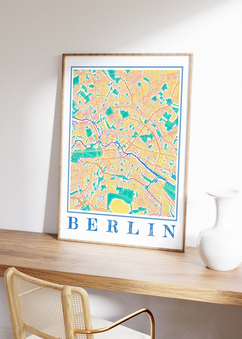 Może przedstawiać: Wydruk w ramie kolorowej mapy Berlina, Niemcy. Mapa jest w odcieniach ż&oacute;łtego, pomarańczowego, zielonego i niebieskiego. Słowo "BERLIN" jest nadrukowane na dole mapy kolorem niebieskim.