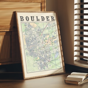 May include: A framed map of Boulder, Colorado, with the city name printed in bold letters at the top. The map is in a light wood frame and is hanging on a wall.