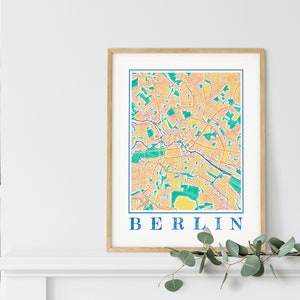 Może przedstawiać: Wydruk w ramie kolorowej mapy Berlina, Niemcy. Mapa jest w odcieniach ż&oacute;łtego, pomarańczowego, r&oacute;żowego, zielonego i niebieskiego. Słowo "BERLIN" jest nadrukowane na dole mapy kolorem niebieskim.