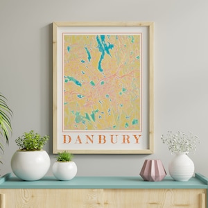 May include: A framed print of a map of Danbury, Connecticut. The map is in a yellow, orange, and green color scheme. The word "Danbury" is printed in orange at the bottom of the print.