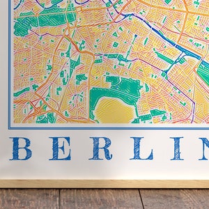 Może przedstawiać: Wydruk w ramie kolorowej mapy Berlina, Niemcy. Mapa jest narysowana w stylu ręcznie rysowanym z kolorystyką tęczy. Słowo "BERLIN" jest napisane na dole wydruku kolorem niebieskim.
