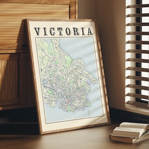 May include: A framed map of Victoria, Australia, with the city name printed in bold black letters at the top. The map is in a light wood frame and is leaning against a wooden cabinet.