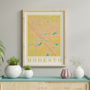 May include: A framed print of a map of Modesto, California. The map is in a yellow, pink, and green color scheme. The word "MODESTO" is printed in gold letters at the bottom of the map.