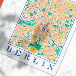 Może przedstawiać: Kolorowa mapa Berlina, Niemcy, z niebieską ramką i napisem "BERLIN" w kolorze niebieskim na dole mapy.
