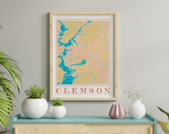 May include: A framed print of a map of Clemson, South Carolina. The map is in a yellow, pink, and blue color scheme. The word "CLEMSON" is printed in orange at the bottom of the print.