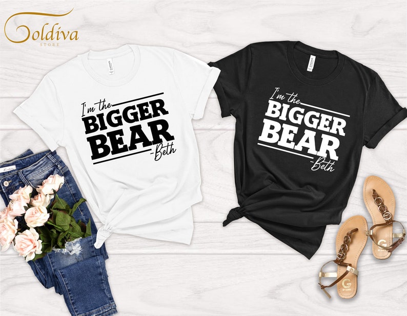 May include: Two t-shirts with the text "I'm the bigger bear - Beth" printed on them. One t-shirt is white and the other is black.